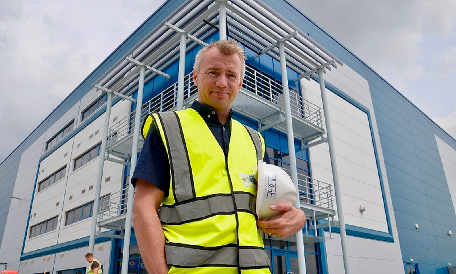 Director Adam Sedgewick, wearing a hi-vis jacket, holding his helmet, standing in front of a building.